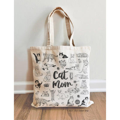 The Sween Shop Cat Mom Canvas Tote Bag is a beige cotton tote featuring black playful cat illustrations and “Cat Mom” in the center—a stylish and reusable accessory perfect for any cat lover.