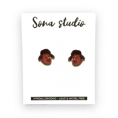 Christmas Cousin Earrings by Sona Studio are handmade, head-shaped earrings with brown hats. Displayed on a branded card, they feature hypoallergenic stainless steel posts and are lead- and nickel-free.