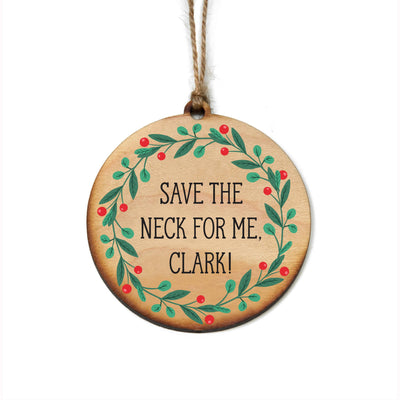 The Driftless Studios Save the Neck for Me Clark Christmas Ornament is a 3.25-inch round wooden piece with a green leaf and red berry wreath, "SAVE THE NECK FOR ME, CLARK!" in black text, and hangs by a brown string.