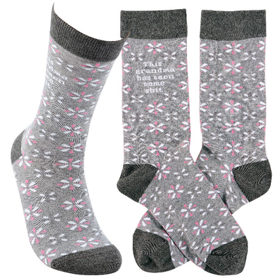 Part of the Trash Talk By Annie Collection, Primitives by Kathys This Grandma Has Seen Socks include three gray socks with pink and white floral patterns. Two are side by side, one angled, and one boldly states This grandma has seen some s**t. They feature dark gray tops, heels, and toes.