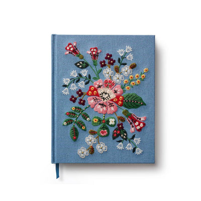 The Gracie Embroidered Sketchbook by Rifle Paper Co. is a blue fabric hardcover journal with vibrant embroidered flowers and leaves on the front, plus a blue ribbon bookmark—ideal for use as a diary or sketchbook.