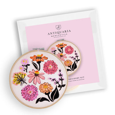 The Antiquaria Zinnia Sampler Premium Embroidery Kit (6 inch) features two wooden hoops with vibrant floral designs, packaged on a pink and white background—perfect for beginner DIY embroidery enthusiasts.