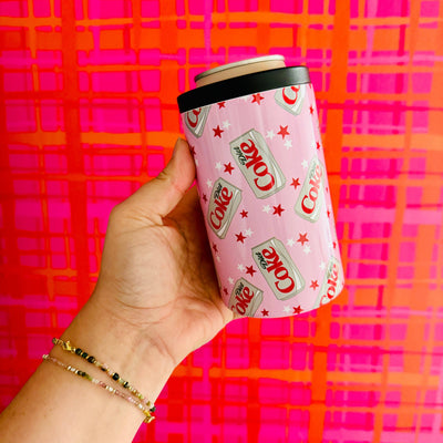 A hand holds the Sonny Rising Pink Diet Coke Inspired Pattern 12 oz Can Cooler, designed with a sweat-free finish and Diet Coke cans with red stars, set against a vibrant pink and orange plaid background.