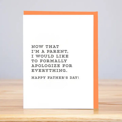 The Formally Apologize Fathers Day Greeting Card by Huckleberry Letterpress is on a wooden table. It features an orange border on the right, and its letterpress printed on premium Mohawk Paper with the humorous message: Now that Im a parent, I would like to formally apologize for everything. Happy Fathers Day!.