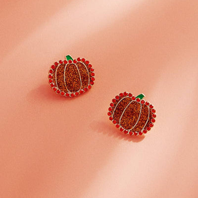 The Thanksgiving Pumpkin Rhinestone Post Earrings by Designature New York feature orange rhinestone pavé and green accents, shown on a soft pink background with gentle lighting.