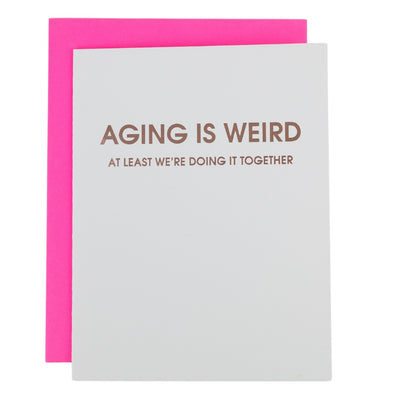 The Chez Gagné Aging is Weird - Letterpress Birthday Card features bright white tree-free paper, rosegold foil text, and comes with a vibrant pink envelope. Text reads: AGING IS WEIRD. AT LEAST WE’RE DOING IT TOGETHER.