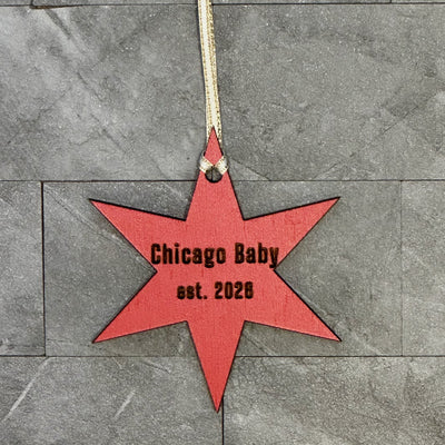 Red star-shaped ornament with 'Chicago Baby est. 2028' text on a gray stone surface