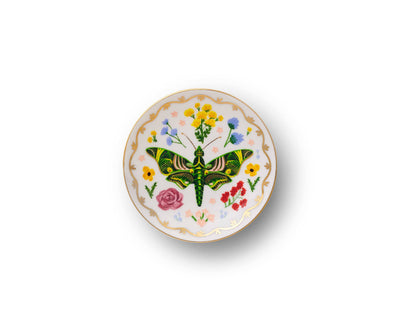 The Curio Porcelain Ring Dish by Rifle Paper features a green butterfly at the center with yellow, pink, and blue flowers, enhanced by metallic gold accents on the rim. This elegant dish from Rifle Paper Co. stands out against its white background.