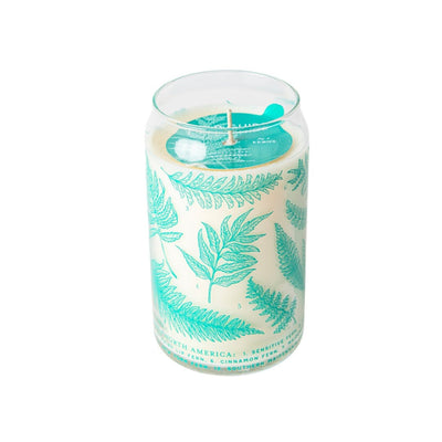 Explore the magic of Good & Well Supply Co.s Ferns Soy Candle from the Forest Floor Collection. This hand-poured blue wax candle is set in a glass jar with green fern designs on a white background. It includes a single wick and is embellished with a charming blue paper boat, offering a serene fragrance experience.
