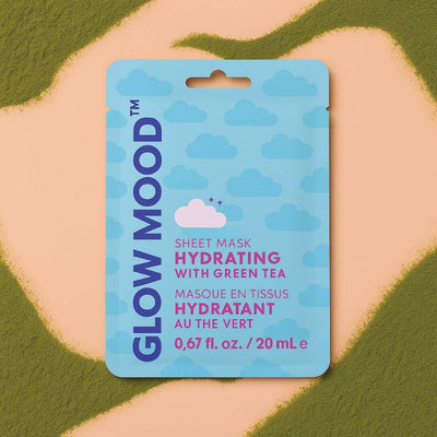 A blue packet of Glow Mood’s Hydrating Sheet Mask with Green Tea, featuring cloud designs, rests on a beige and green abstract background—an ideal addition to your nighttime skincare routine.
