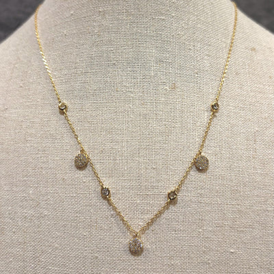 The Sirens Song Charm Necklace by Golden Stella features a delicate gold-dipped adjustable chain with small round, sparkling stone pendants, displayed on a beige fabric bust.