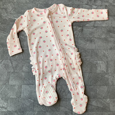 The Strawberry Swiss Dot Ribbed Two-Way Ruffle Back Zipper Footie by Angel Dear, a cozy pink polka-dotted onesie with long sleeves and footies, lies on a textured gray surface, featuring a front zipper with zipper guard and side ruffles for comfort.