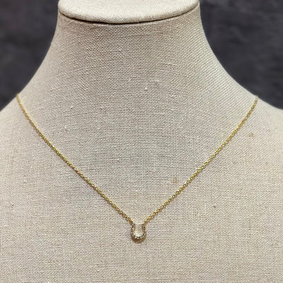 The Golden Stella horseshoe stone necklace is a delicate gold-dipped, adjustable piece with a small horseshoe-shaped pendant, shown on a beige fabric-covered jewelry bust.