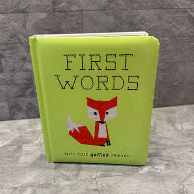 First Words With Cute Quilted Friends by Penguin Random House LLC features a green cover with a geometric red fox and the subtitle with cute quilted friends. The book stands on a gray textured surface—ideal for fans of urban quilting.