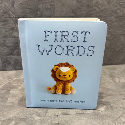The book First Words With Cute Crochet Friends by Penguin Random House LLC features adorable crochet animals on a light blue and textured gray cover, making it a charming first words book for children.