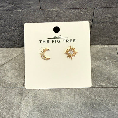 Star and Moon Mismatched Stud Earrings by BETTYOH INC are shown against a gray tile background, featuring a crystal crescent moon stud and a starburst stud with a central gem.