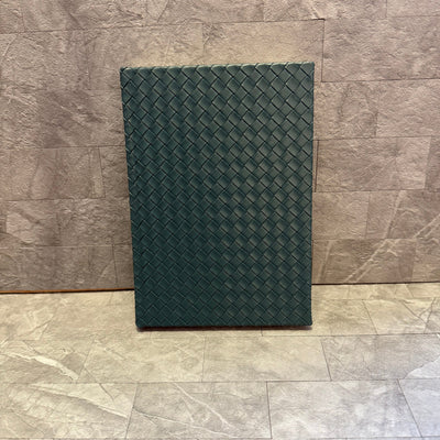 The Punch Studio Woven Vegan Leather Journal in teal stands upright against a textured gray stone wall and floor.
