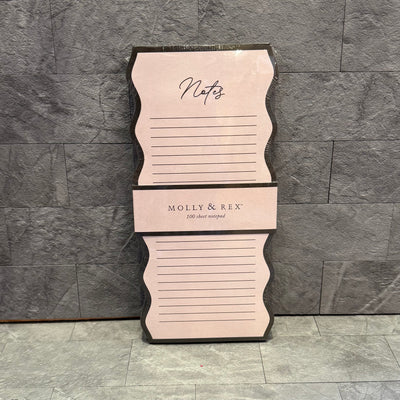 A Magnetic List Pad Blush by Punch Studio with wavy pink edges and Notes at the top, shown on a gray stone tile background. This lined notepad has 100 sheets for writing.