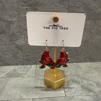 Christmas Cardinal Bird Earrings by Golden Stella, measuring 1.5" long, feature red cardinals with green leaves and red berries. Displayed on a gold stand with THE FIG TREE card, set against a gray tiled background.