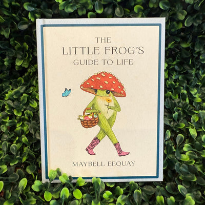 The Little Frog's Guide To Life by Hachette Book Group is an inspirational gift celebrating self-love, featuring a green frog in boots with a basket and red mushroom umbrella, surrounded by greenery and a blue butterfly.