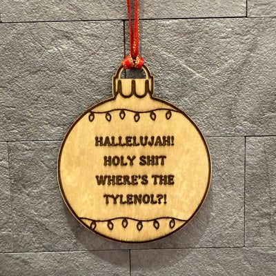 The Jim Harris Where's the Tylenol?! Ornament is a birch laser-engraved ornament with festive light border and “HALLELUJAH! HOLY SHIT WHERES THE TYLENOL?!” text, shown hanging by string against a gray tiled wall.