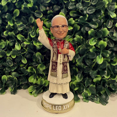 The Pope Leo XIV Mini Bobblehead by the National Bobblehead Hall of Fame and Museum shows the bespectacled pope in papal robes, holding a red book and raising one hand in blessing—an exclusive American Pope collectible.