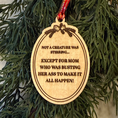 The Not a Creature was Stirring Ornament by Jim Harris hangs on the tree with “NOT A CREATURE WAS STIRRING... EXCEPT FOR MOM WHO WAS BUSTING HER ASS TO MAKE IT ALL HAPPEN!” and features laser-engraved pine branch decorations on top.