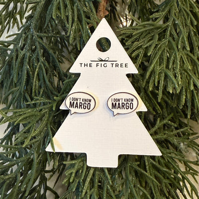 A pair of "I Don’t Know Margot" earrings by Sona Studio are displayed on a Christmas tree-shaped card among green pine branches. The card notes that the stainless steel earrings are lead and nickel free.
