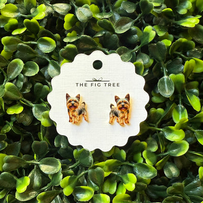 Yorkshire Terrier Post Earrings by BETTYOH INC, displayed on a scalloped white card, are lead- and nickel-free—ideal for dog lovers with sensitive ears. The card is shown against a backdrop of green leaves.