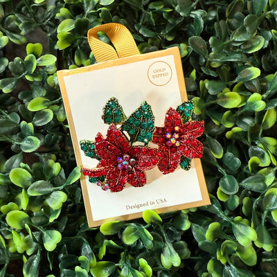 The Golden Stella poinsettias brooch is a 2-inch gold-plated jeweled piece with red flowers and green leaves, presented on a "Gold Dipped & Designed in USA" card—an elegant addition to any collection.