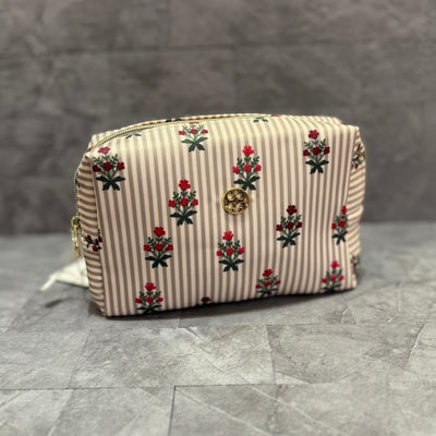 The Let's Face It Mini Cosmetic Travel Bag in Cottage Stripes by Mary Square features beige and white vertical stripes with red and green floral accents, a gold front emblem, and offers compact organization for travel essentials. Shown on gray tiles.
