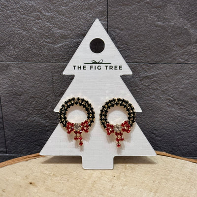 Golden Stella's sparkling wreath Christmas earrings, featuring red bows and crystal posts, are displayed on a tree-shaped card labeled The Fig Tree against a textured gray background.