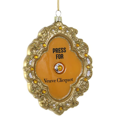 The Cody Foster Press for French Champagne Ornament is a 3.5-inch gold and orange jeweled decoration with floral designs, "PRESS FOR Veuve Clicquot" text, a central button, and hangs by a gold string.