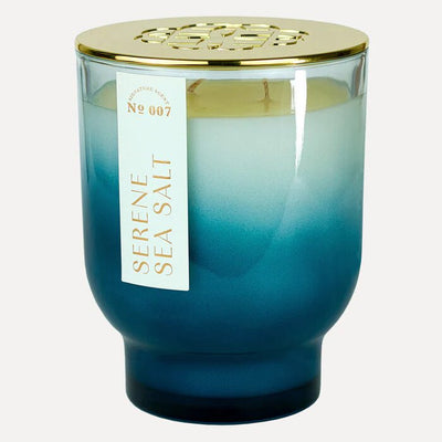 The Serene Sea Salt 21 oz Maeve Glass Candle by Elum is a blue ombre candle jar with gold geometric lid design, crafted using Aura Pure technology and filled with light-colored wax for ultimate serenity and relaxation.