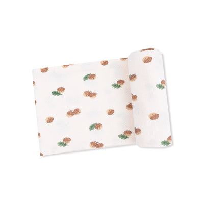 The Angel Dear Tiny Acorns Bamboo Stretch Knit Swaddle Blanket features a white background with small brown acorns and green leaves in a repeating pattern, shown partially unrolled.