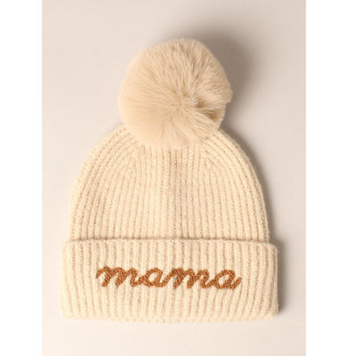 The Mama Script Embroidered Pom Beanie in Oatmeal by Fashion City features a cream-colored knit design with a large faux fur pom-pom, brown cursive mama embroidery on the folded brim, and is one-size-fits-most. The hat is displayed flat on a light background.