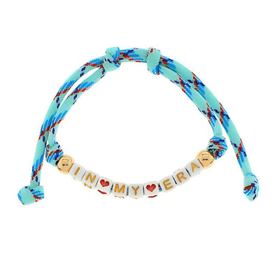 The Golden Stella In My Era Friendship Bracelet features blue and red braided string, white plastic beads with gold edges spelling IN MY ERA, red heart beads between words, and an adjustable knot closure for a perfect fit.