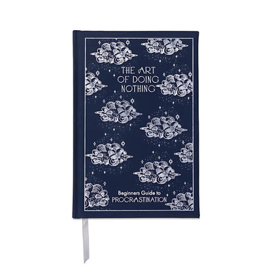 The Art of Doing Nothing Journal by Designworks Ink is a navy blue bookcloth notebook with white clouds and stars, cover text "The Art of Doing Nothing" and "Beginners Guide to Procrastination," plus a white ribbon bookmark.