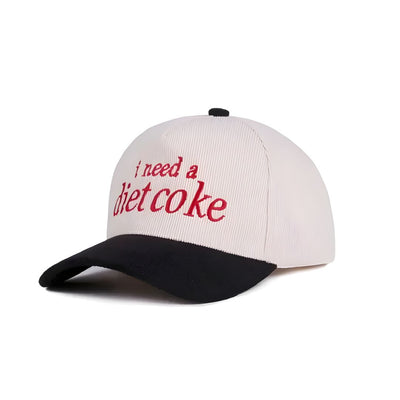 The 42POPS I Need a Diet Coke Two Tone Corduroy Cap is a white and black baseball cap with red "i need a diet coke" text on the front, plus an adjustable strap with metal buckle for a perfect fit.