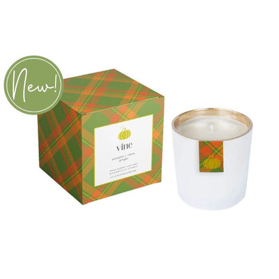 The Vine Boxed Candle by Annapolis Candle features white soy wax in a glass container with a matching box adorned with green-orange plaid and a pumpkin design. Both display the Vine label. A green circle says "New! Perfect for holiday festive fragrances.