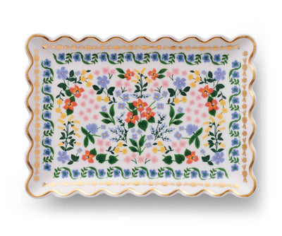 The Wildwood Porcelain Catchall Tray by Rifle Paper Co. is a rectangular plate with wavy edges, showcasing orange, pink, yellow, and purple flowers with green leaves, accented by a metallic gold border.