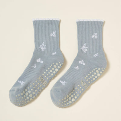Effortless Club’s Snowflake Petal Grip Sock [Denim]: light blue organic cotton socks with white floral patterns, scalloped white cuffs, beige non-slip grips, and a cushioned footbed for comfort.