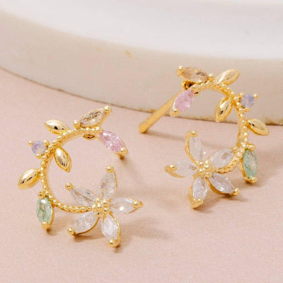 Titania Flower Circle Stud Earrings by Fame Accessories feature gold-dipped crescent moon shapes with leaf and flower designs, adorned with pink, green, purple, and clear cubic zirconia gemstones, displayed on a light surface.