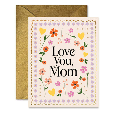 The Mosaic Mom Floral Greeting Card by Ginger P. Designs features flowers and hearts in vibrant red, orange, yellow, and purple. Love You, Mom is boldly displayed on the front. It comes with an antique gold shimmer envelope peeking from behind.