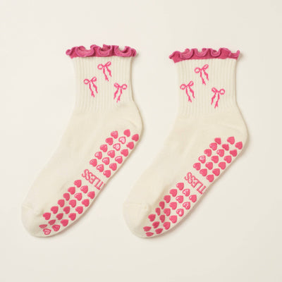 Effortless Clubs Bow Ruffle Grip Sock (Hot Pink) features white Pilates socks with pink ruffled cuffs, side bow patterns, and pink heart-shaped non-slip grips on the soles for comfort.