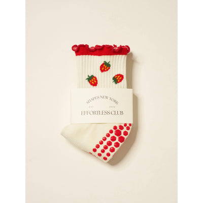The Strawberry Ruffle Grip Sock by Effortless Club features white fabric with red ruffled cuffs, strawberry patterns, red grip dots on the sole, a cushioned footbed for comfort, and a SLIPPES NEW YORK EFFORTLESS CLUB label.