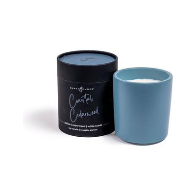 The Earth & Ember 13 oz Candle: Coastal Cedarwood from Milkhouse Candle Company features blue soy wax in a matching holder and comes in black cylindrical packaging—an ideal gift candle for any occasion.
