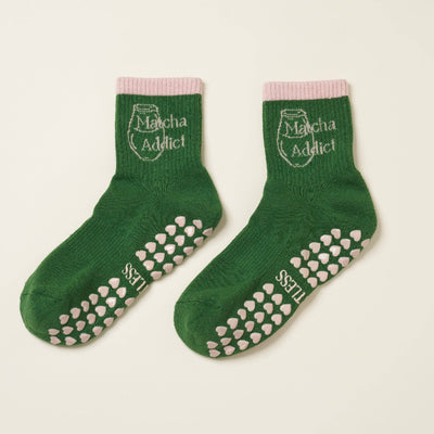 The Matcha Addict Grip Sock by Effortless Club features green organic cotton with pink grips and cuffs, Matcha Addict text, and a matcha cup image on the ankle—perfect for Pilates and matcha lovers.