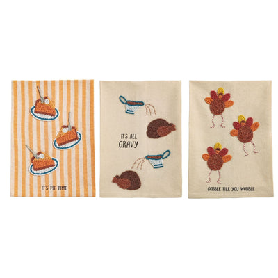 Mud Pie’s Beaded Thanksgiving Towels set includes three cotton towels: one with pie and "It's Pie Time," one with gravy over turkey and "It's All Gravy," and one with two turkeys and "Gobble Till You Wobble," all with beaded appliqués.