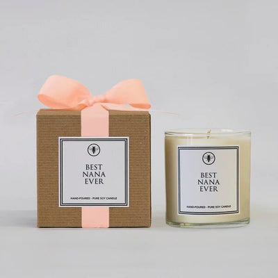 The Best Nana Ever Boxed Candle by Ella B features a soy candle in a glass holder beside a brown box with a pink ribbon, both labeled Best Nana Ever. Crafted from pure soy wax, it offers the soothing Sea Mist & Jasmine scent against a light gray background.